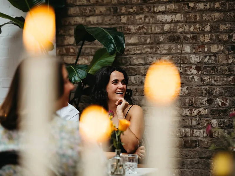 A guest laughing during a candlelit dinner at The Hackney, brick wall and greenery behind