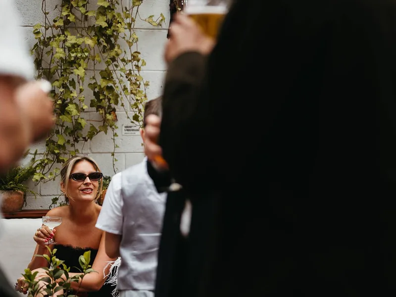 A guest with a cocktail in the courtyard at The Hackney, ivy and ferns behind